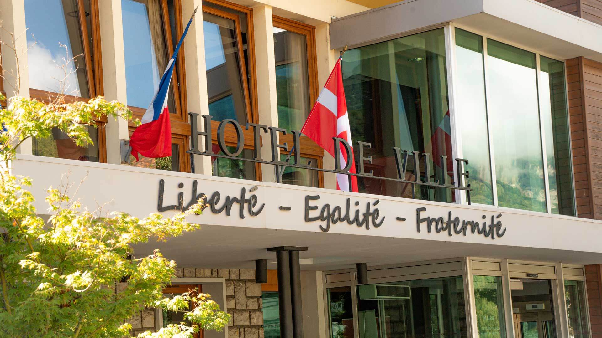 Photographie du fronton de la mairie avec le slogan de la république française : Liberté - Égalité - Fraternité.Photographie aérienne du centre ville d'Aime-la-Plagne.