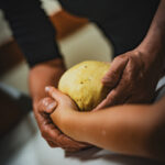 Mains d'un boulanger accompagnant les mains d'un enfant à former une boule de pâte pour en faire du pain