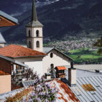 Vue sur les toits et sur l'église de Tessens, avec le village de Macôt et des montagnes enneigés en arrière plan