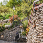 Ruelle entouré de murets en pierres, de jardin fleuris et d'un lampadaire, à Tessens, vue en contre-plongée à ras du sol