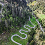 Vue aérienne sur des virages en lacets entourés de forets de sapin, un ciel nuageux au loin