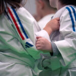 Deux enfants en uniforme blanc de judo s'agrippent à la manche de l'autre pendant l'entraînement.