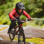 Un jeune enfant portant un casque et un maillot rouge fait du vélo BMX sur le pump track d'Aime.