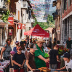 Des personnes et des enfants s'amusent lors des jeudis d'Aime dans la grande rue, avec des banderoles colorées au-dessus de leur tête.