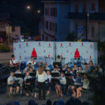 Concert nocturne en plein air avec un chef d'orchestre dirigeant un groupe de musiciens, se produisant devant un public.