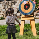 Une jeune fille se tient face à une cible sur laquelle sont épinglés des ballons, en plein air, par une journée ensoleillée.