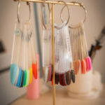 Échantillons de couleurs de vernis à ongles sur des anneaux de présentation, suspendus à un support doré sur une table.
