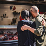Un couple se tenant par le bras se tient devant le comptoir d'un boucher, regardant la viande exposée.