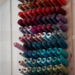 Des bobines de fil de différentes couleurs sont disposées sur un support mural.