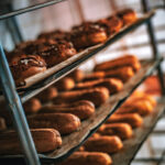 Rangées d'éclairs et de pâtisseries fraîchement cuits refroidissant sur des grilles métalliques dans une boulangerie.