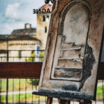 Peinture rustique d'une porte cintrée sur un chevalet, avec la basilique visible à travers une fenêtre.