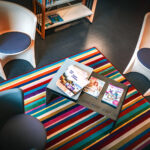 Trois chaises modernes entourent une petite table avec des magazines, sur un tapis rayé coloré dans une pièce confortable.