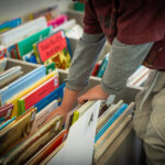 Enfant feuilletant des livres colorés dans une boîte de bibliothèque étiquetée avec des séparateurs alphabétiques.