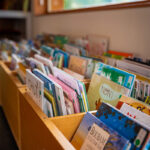 Des bacs en bois remplis de livres pour enfants colorés à côté d'une fenêtre avec vue sur les montagnes.