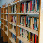 Étagères remplies de livres colorés à la médiathèque de Centron, avec des œuvres d'art exposées sur les étagères supérieures.