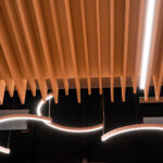 Plafond moderne avec des lattes en bois et des luminaires LED incurvés et lumineux dans un espace intérieur minimaliste.