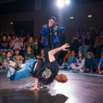 Un breakdancer se produit sur une seule main devant une foule enthousiaste lors d'un événement en salle.