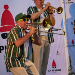 Deux musiciens en tenue assortie jouent du trombone et de la trompette sur scène devant une toile de fond au couleur de La Plagne.