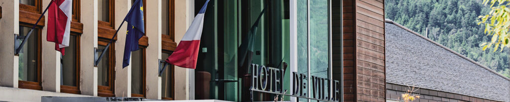 Façade de la mairie d'Aime avec l'enseigne écrit "Hôtel de Ville" et les drapeaux de la Savoie, de l'Europe et de la France