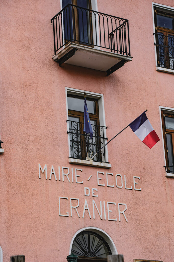 Façade d'un bâtiment rose avec l'enseigne "Mairie / École de Granier" et les drapeaux de l'Europe et de la France