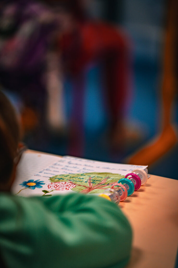 Enfant devant un cahier avec des écritures et des dessins d'arbre et de fleurs