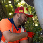 Employé de la régie des eaux, avec une casquette de la 6000D, en train de réparer un tuyau au milieu de la forêt
