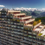 Bâtiment en gradins avec balcons, adossé à des montagnes enneigées sous un ciel bleu limpide.