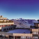 Vue par dessus le paquebot des neiges à Aime 2000 avec le mont Blanc au loin et des montagnes enneigées sous un ciel bleu clair.