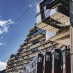 Bâtiment d'une station de ski avec un téléphérique passant devant sous un ciel bleu éclatant.