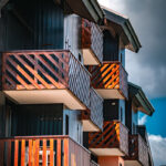 Balcons en bois avec garde-corps sur un bâtiment moderne, sous un ciel partiellement nuageux.