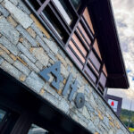 Bâtiment moderne en pierre avec une grande enseigne Alto et des fenêtres supérieures en bois, photographié en contre-plongée.