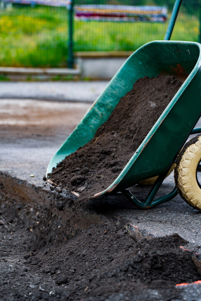 Brouette déversant de la terre dans un trou creusé dans le bitume