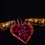 L'ornement en forme de cœur rouge avec des lumières est suspendu entre deux branches enveloppées de guirlandes lumineuses dorées la nuit.