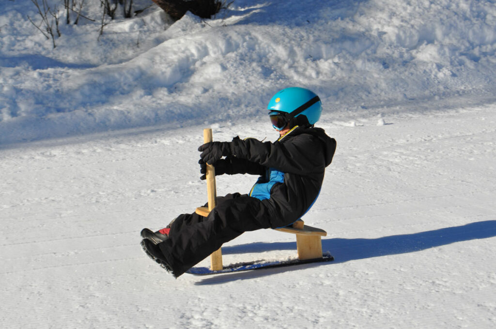 Un jeune garçon avec casque, masque et combinaison de ski descend la piste l'espace nordique de Prachanier à Granier sur son paret