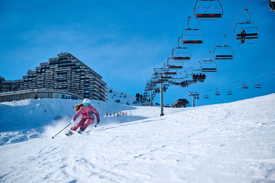 Skieuse descendant la piste devant l'immeuble "le paquebot des neiges" à Plagne Aime 2000