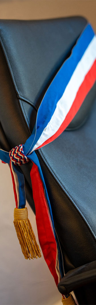 Sur un fauteuil en cuir noir repose une écharpe de Maire aux couleurs du drapeau français, bleu, blanc et rouge